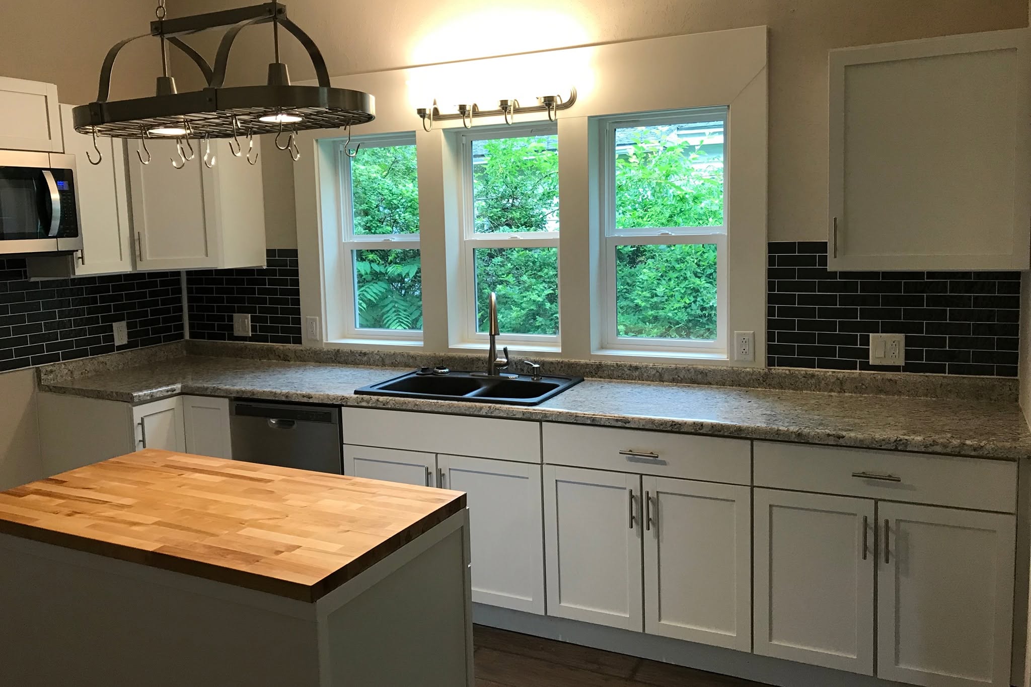 Finished kitchen in the College Street historic renovation - white cabinets, butcher-block island, and black subway tile backsplash